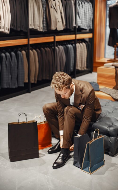 Sale, shopping, fashion, style and people concept. Elegant young man choosing footwear in mall.